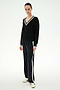 Wearing the SPLITS59 Jemma Knit V Neck in Black/White, this person pairs the soft rayon sweater featuring white trim with black wide-leg pants with side stripes and white sneakers, standing against a plain light background.