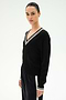 A woman stands against a plain, light background wearing the SPLITS59 Jemma Knit V Neck in Black/White—a soft rayon-nylon sweater featuring a white-trimmed V-neck—paired with matching black pants accented by a white stripe.