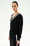 A woman stands against a plain, light background wearing the SPLITS59 Jemma Knit V Neck in Black/White—a soft rayon-nylon sweater featuring a white-trimmed V-neck—paired with matching black pants accented by a white stripe.