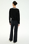 A person with dark hair in a bun stands facing away, wearing the SPLITS59 Jemma Knit V Neck in Black/White—a long-sleeve top paired with wide-leg black pants featuring white side stripes, all crafted from soft rayon fabric—against a plain white background.