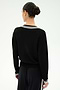 A person stands facing away, wearing the SPLITS59 Jemma Knit V Neck in Black/White paired with black soft rayon pants. Their hair is tied back in a neat bun, and the background is plain white.
