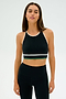 A person wearing the SPLITS59 Layla Airweight Bra in Black/Arugula stands against a plain background, fully dressed in an athletic ensemble.