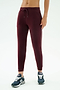 A person wears SPLITS59’s Airweight Jogger 7/8 with Piping in Dark Cherry/Indigo and dark blue sneakers, standing against a plain white background.