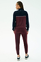 A person with braided hair faces away, wearing the SPLITS59 Millie Airweight Half Zip in Dark Cherry/Indigo and athletic shoes, shown against a plain white background.