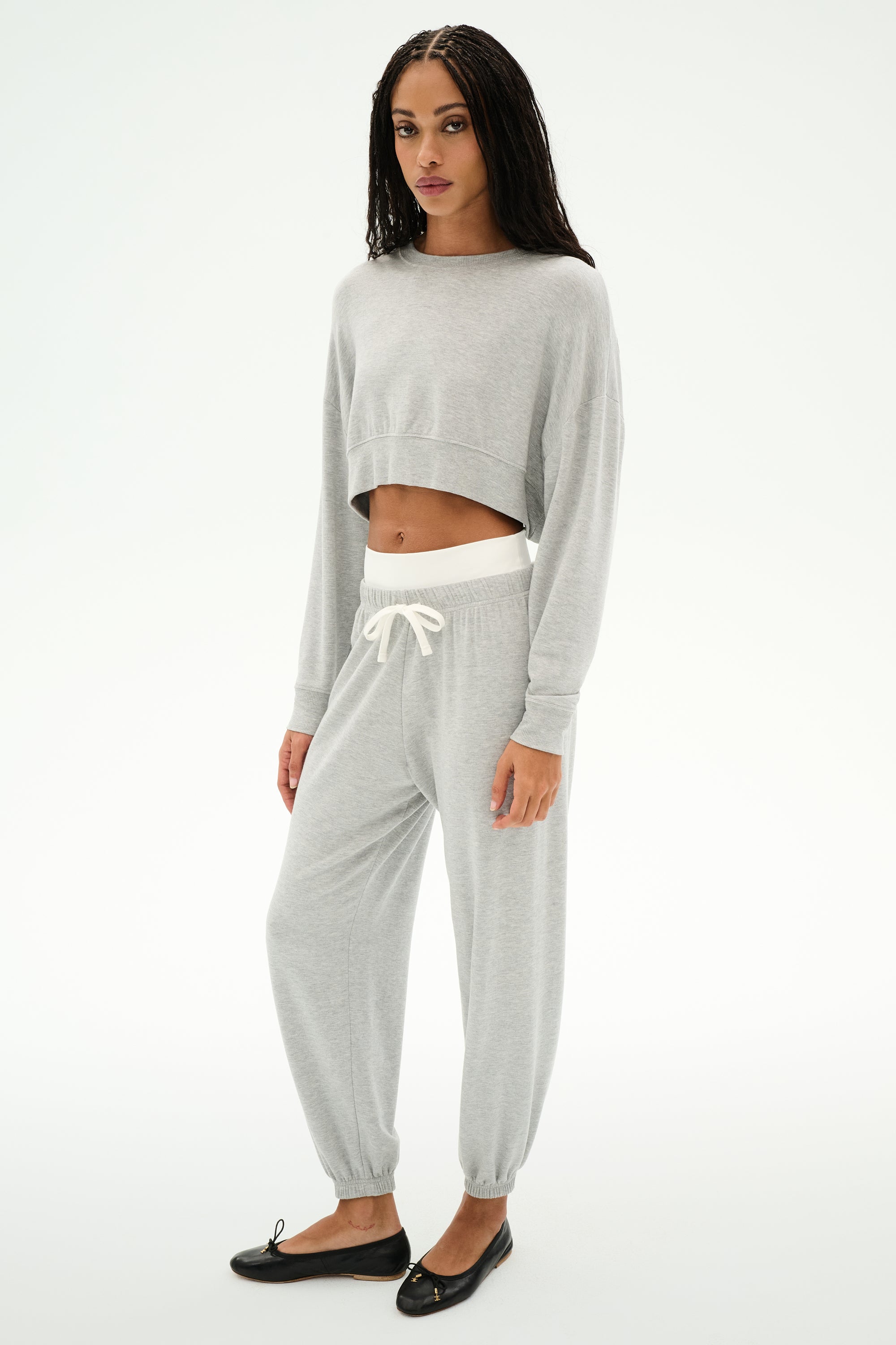 A woman wears SPLITS59’s Andie Dual Waist Sweatpant in Heather Grey/White—a soft, cropped jogger crafted from a modal-spandex blend—paired with black flats, set against a plain white background.