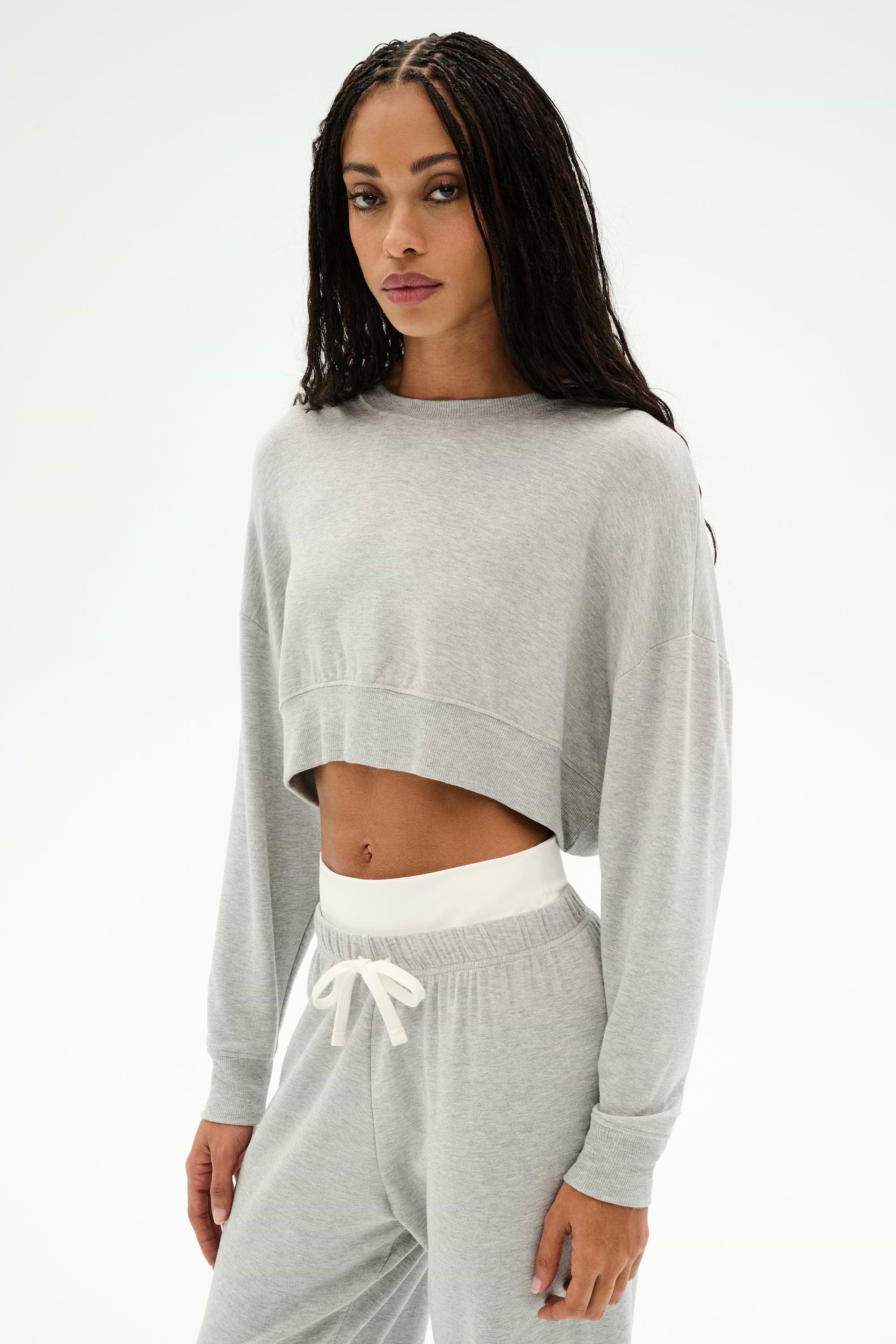 Model wears the SPLITS59 Noah Fleece Crop Sweatshirt in Heather Grey, paired with matching sweatpants featuring white drawstrings, all crafted from soft modal spandex, posed against a plain white background.