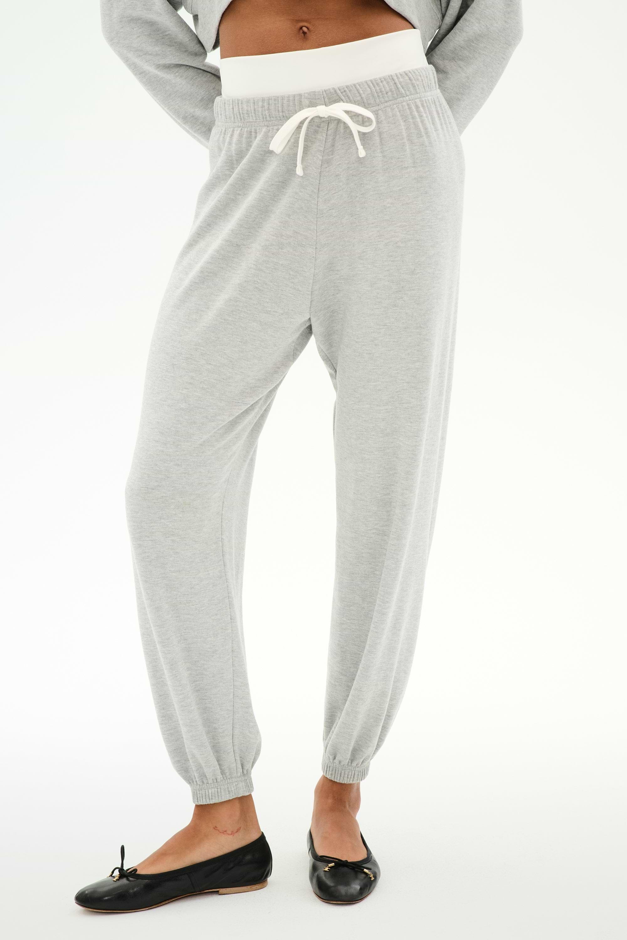 A person wears the SPLITS59 Andie Dual Waist Sweatpant in Heather Grey/White featuring a visible white waistband and white drawstring, paired with black ballet flats, standing against a plain background.