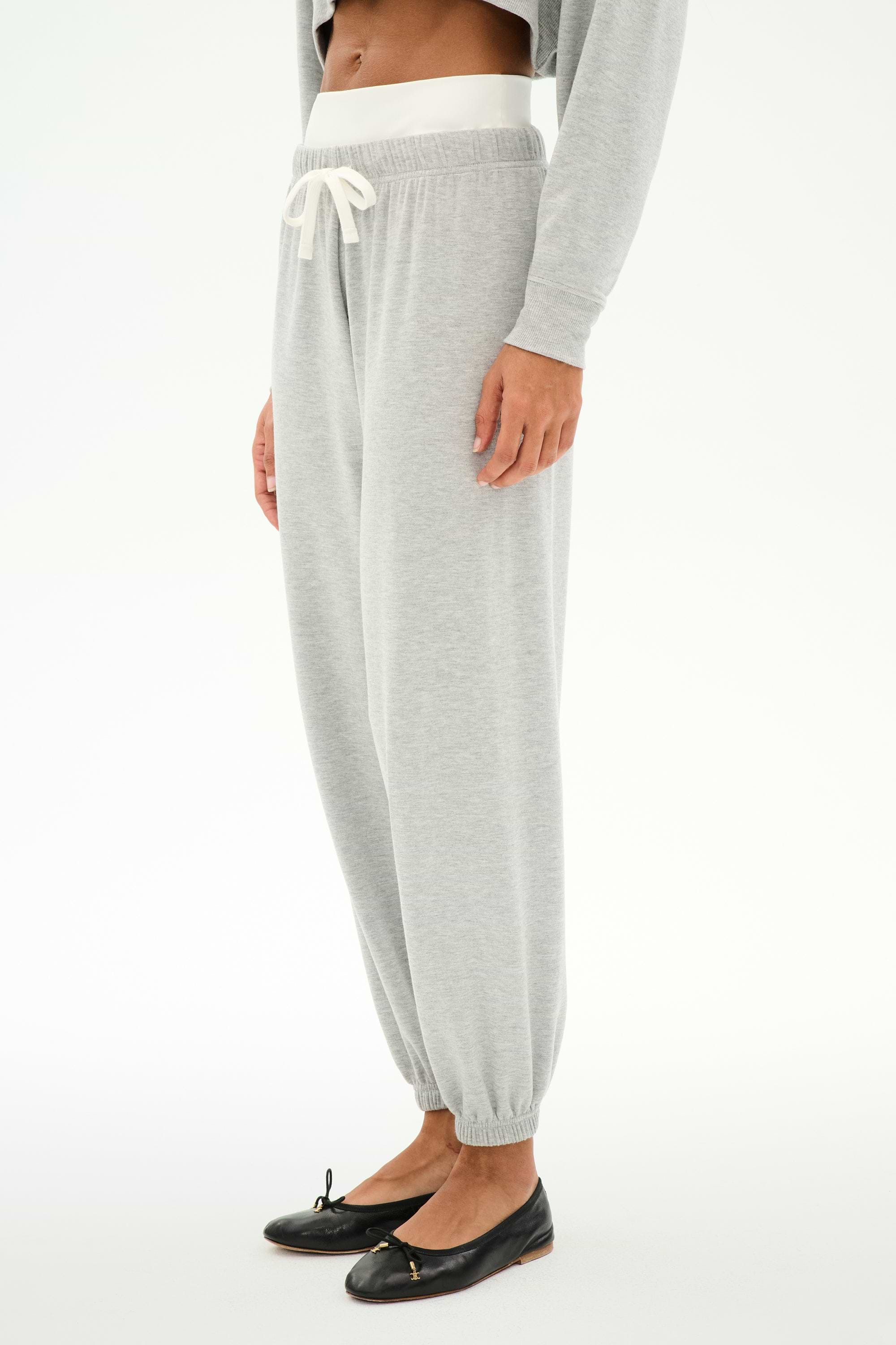 A person wears the SPLITS59 Andie Dual Waist Sweatpant in Heather Grey/White, featuring a white drawstring, paired with a gray top and black ballet flats, standing against a white background.