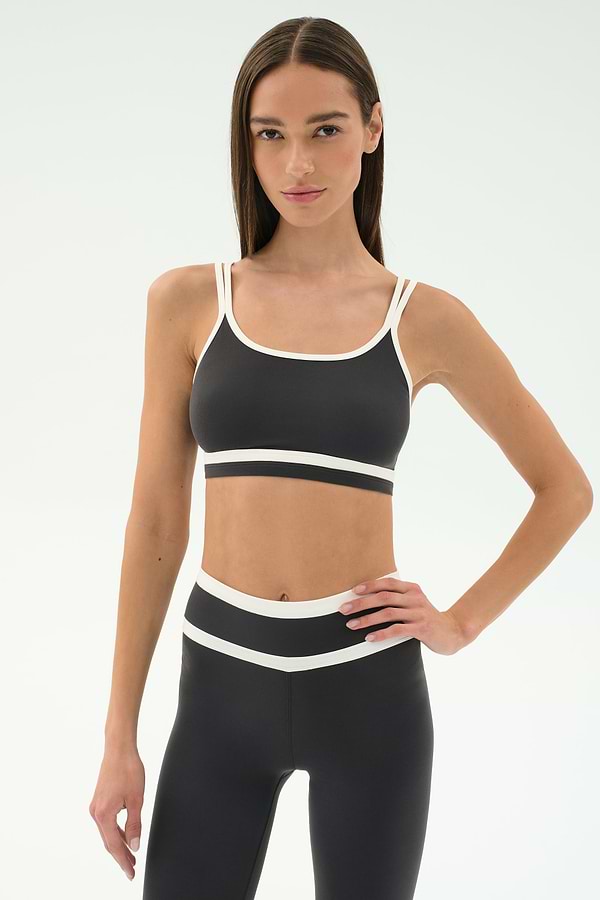 Woman wearing the SPLITS59 Eva Rigor Double Strap Bra in Graphite/White, standing with one hand on her hip against a plain background—ideal activewear for gym workouts.