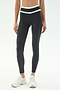 A person wearing SPLITS59 Mason High Waist Rigor Full Length leggings in Graphite/White with a white waistband and white athletic shoes stands on a plain background.