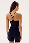 A woman with long hair faces away, wearing a body-hugging black Airweight 6” Short Jumpsuit - Black by SPLITS59, perfect for hot yoga, against a plain background.