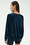 A woman with straight brown hair is seen from behind wearing the SPLITS59 Joy Velour Crewneck in Indigo and black shorts against a plain light background.