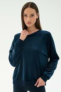 A woman wears the SPLITS59 Joy Velour Crewneck in Indigo with black leggings, standing against a plain white background.