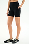 A person wears SPLITS59 Airweight High Waist Pocket Short 6” in black with black Adidas sneakers, standing against a plain white background.