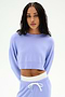 A woman wears the SPLITS59 Noah Fleece Crop Sweatshirt in Purple Haze, paired with matching stretchy sweatpants featuring a white drawstring, standing against a plain white background.