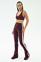 A woman stands against a plain background wearing SPLITS59's Raquel High Waist Flared Legging in Dark Cherry/Creme, styled with a matching burgundy sports bra and burgundy sneakers.