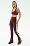 A woman stands against a plain background wearing SPLITS59's Raquel High Waist Flared Legging in Dark Cherry/Creme, styled with a matching burgundy sports bra and burgundy sneakers.