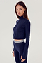 Front view of woman with brown straight hair wearing a dark blue cropped sweatshirt with collar, and dark blue leggings with white and dark blue stripes on the waistband
