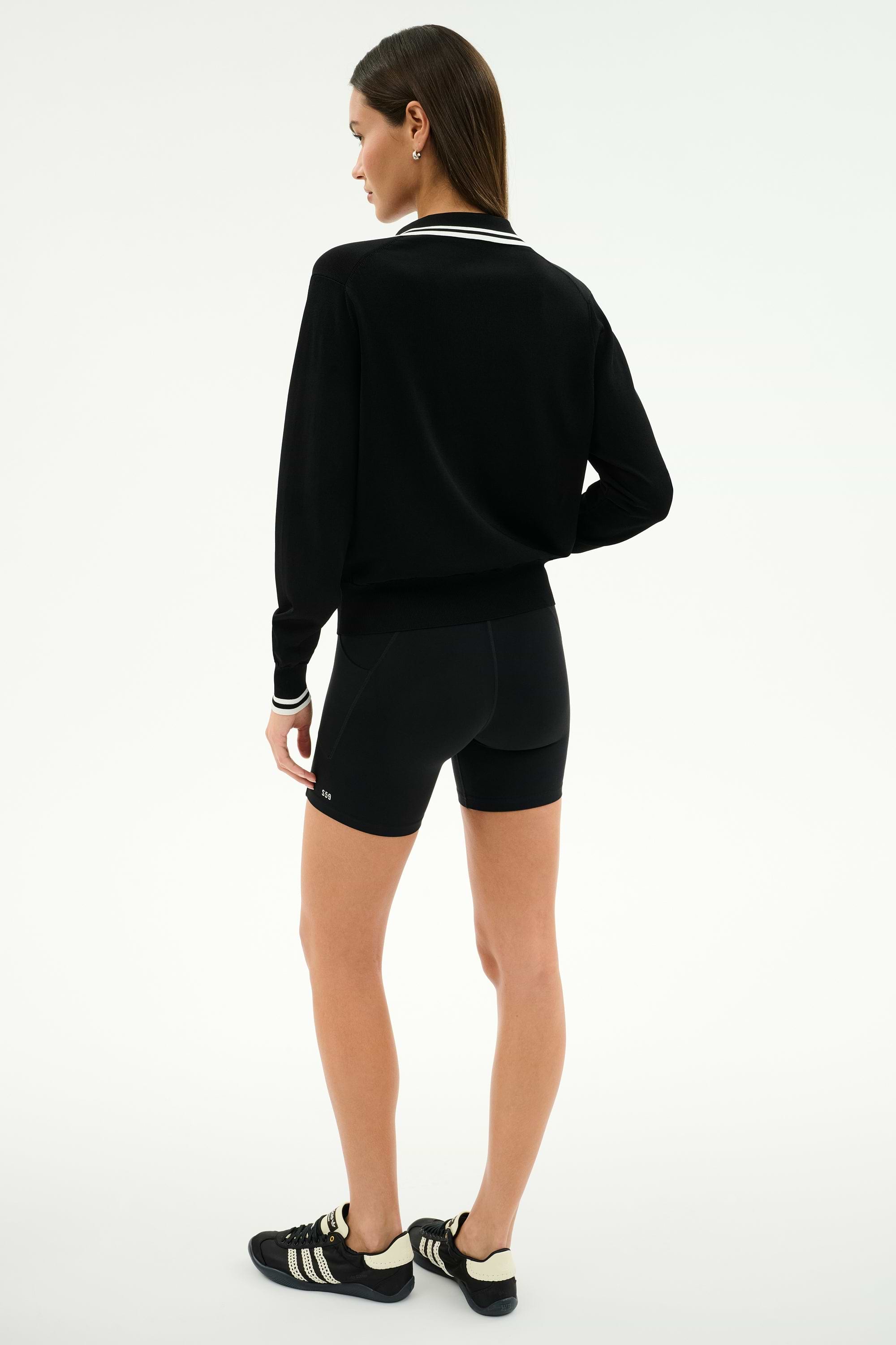 A woman stands facing away, wearing the SPLITS59 Taylor Knit Polo in Black/White against a plain white background.