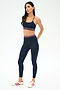 A woman stands in a studio wearing the SPLITS59 Cali Active Rib Bra in Heather Indigo, styled with white sneakers featuring red stripes and an athletic outfit with red, white, and blue accents for comfort and style.