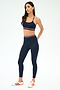 A woman stands in a studio wearing the SPLITS59 Cali Active Rib Bra in Heather Indigo, styled with white sneakers featuring red stripes and an athletic outfit with red, white, and blue accents for comfort and style.