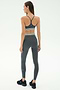 A woman faces away, wearing the SPLITS59 Bailey Active Rib High Waist 7/8 leggings and sports bra set in heather grey with white stripes, paired with black sneakers, against a plain light background.