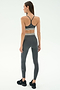 A woman faces away, wearing the SPLITS59 Bailey Active Rib High Waist 7/8 leggings and sports bra set in heather grey with white stripes, paired with black sneakers, against a plain light background.