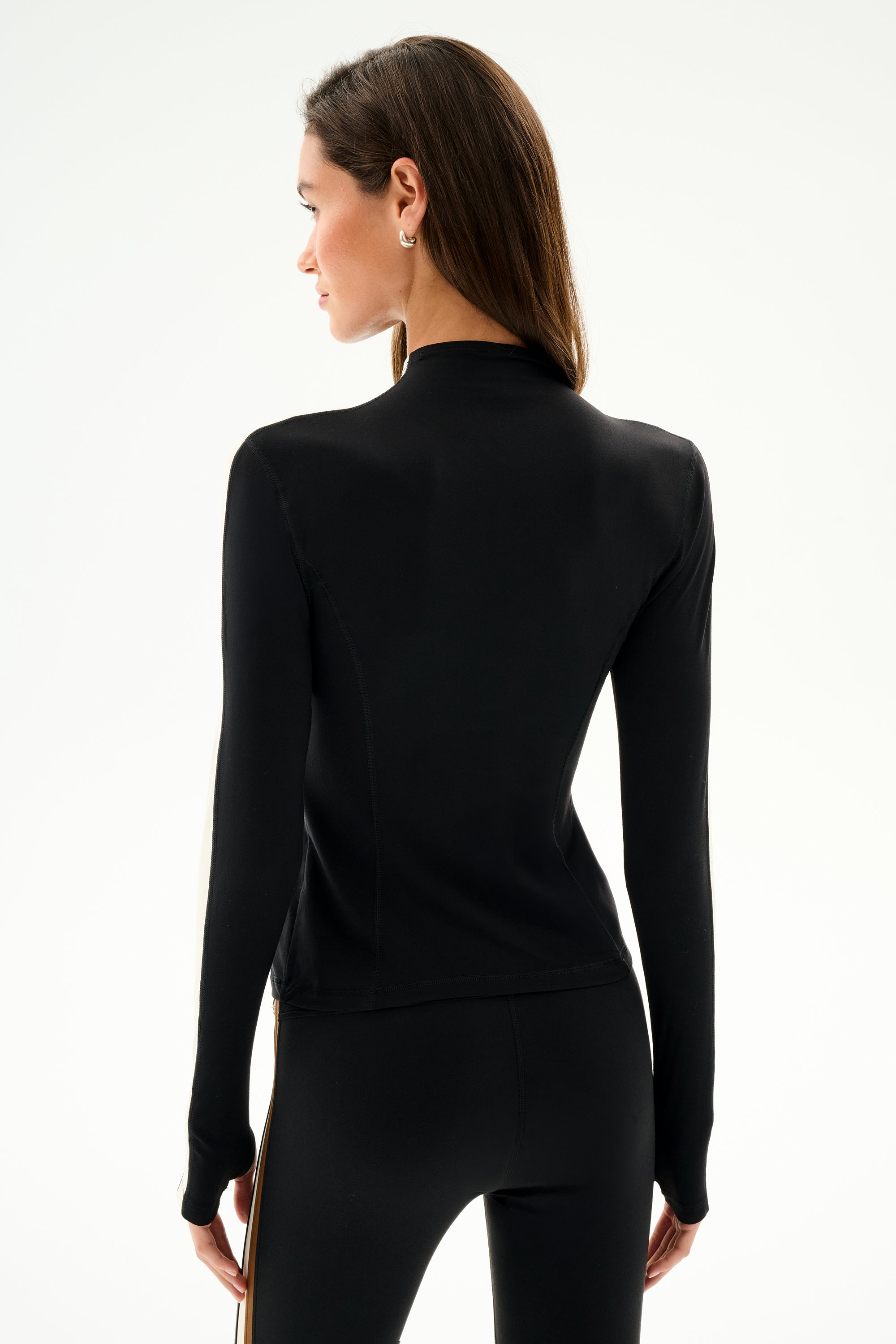 A woman with straight brown hair wears the SPLITS59 Isabelle Airweight Lite Mock Neck - Black/Creme, facing away from the camera against a plain light background.