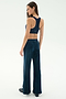 A woman faces away in SPLITS59 Joy Velour Pant in Indigo and a navy sports bra with black shoes, set against a plain light background.