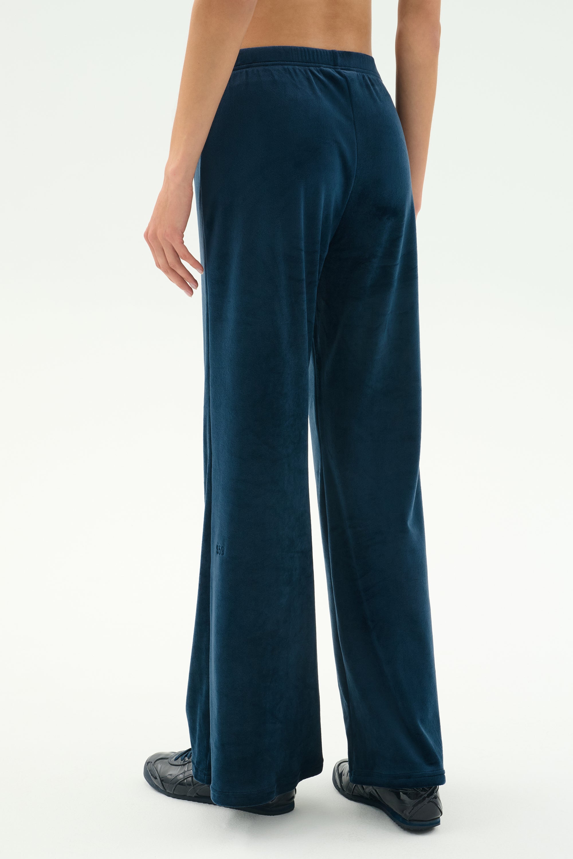 Model wears the SPLITS59 Joy Velour Pant in Indigo, styled with black shoes, photographed from the back against a plain white background.