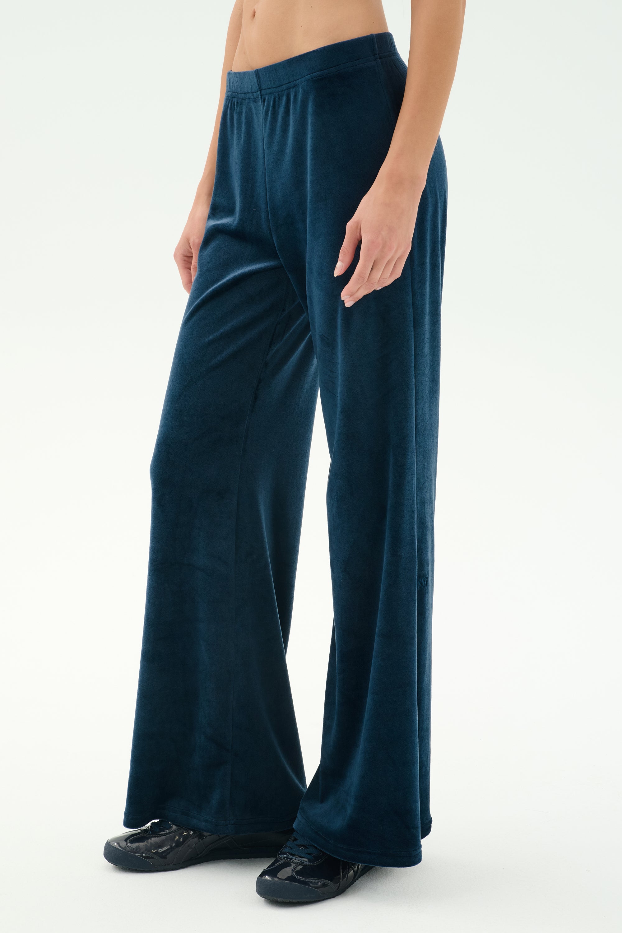 Someone wears SPLITS59 Joy Velour Pant in indigo, styled with black sneakers, standing against a plain light background.