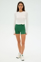 A woman wearing the SPLITS59 Louise Rib Long Sleeve in white pairs it with green shorts and sleek white sneakers, ready for her gym workouts against a plain background.