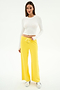 A woman stands in a studio wearing the SPLITS59 Louise Rib Long Sleeve Crop in white, paired with yellow wide-leg drawstring pants and white sneakers—an ideal gym-ready look—against a plain white background.