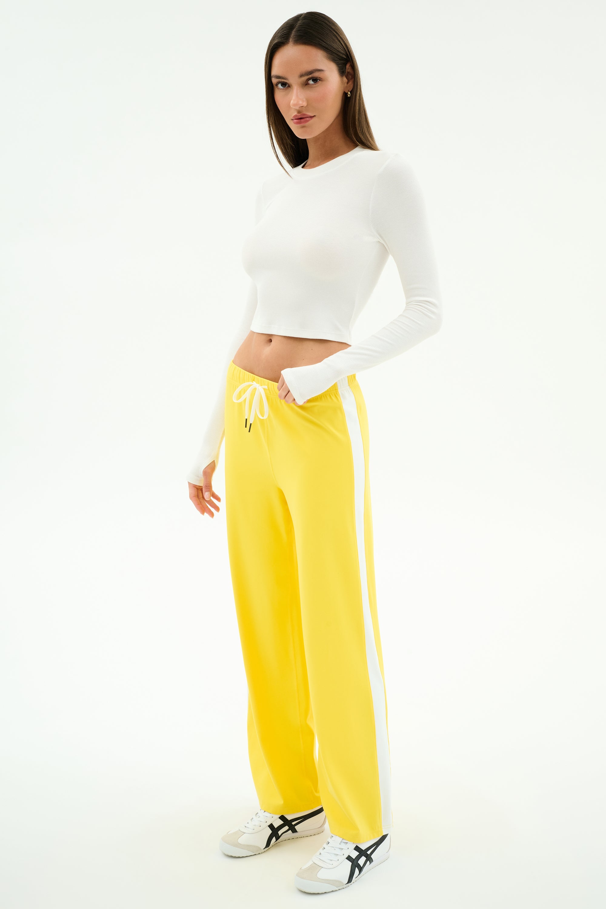 A woman stands against a white background wearing the SPLITS59 Louise Rib Long Sleeve Crop in white—an effortless gym-ready look.