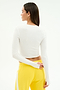 A person with straight brown hair wears the SPLITS59 Louise Rib Long Sleeve Crop in White and yellow pants, standing against a white background facing away and looking to the side.