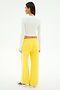 A person stands facing away, wearing the SPLITS59 Louise Rib Long Sleeve Crop in white with bright yellow wide-leg pants and white sneakers featuring black accents, posed against a plain light background. Perfect style for post-gym workouts.