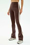 A person wears SPLITS59's Raquel High Waist Flared Legging in Dark Chocolate/Creme, featuring a comfy nylon-spandex blend and white side stripe, paired with gray sneakers against a light background.