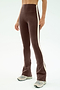 A person wears SPLITS59's Raquel High Waist Flared Legging in Dark Chocolate/Creme, featuring a comfy nylon-spandex blend and white side stripe, paired with gray sneakers against a light background.