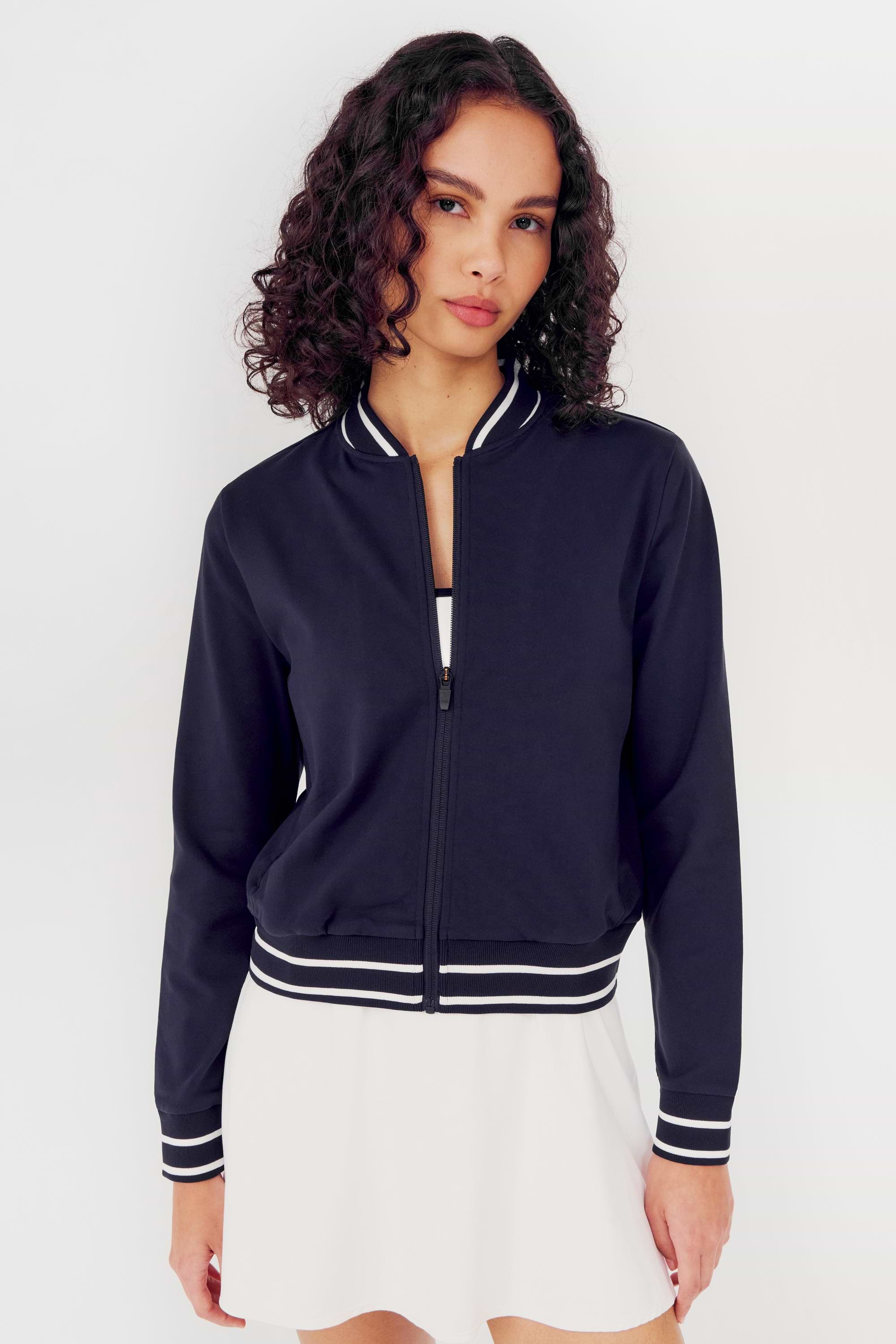 Woman wearing an Ever Supplex Jacket in Indigo by SPLITS59 with white trim and a white spandex skirt.