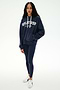 A woman stands facing forward, wearing the SPLITS59 Stella French Terry Oversized Hoodie in Indigo/Splits59 Los Angeles, crafted from soft cotton fabric. She pairs it with navy leggings and white sneakers against a plain white background.