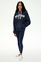A woman stands facing forward, wearing the SPLITS59 Stella French Terry Oversized Hoodie in Indigo/Splits59 Los Angeles, crafted from soft cotton fabric. She pairs it with navy leggings and white sneakers against a plain white background.
