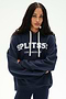 A woman stands with arms crossed against a plain background, wearing the SPLITS59 Stella French Terry Oversized Hoodie in Indigo—a soft 100% cotton piece featuring "SPLITS59 LOS ANGELES" printed on the front.