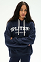 A woman stands with arms crossed against a plain background, wearing the SPLITS59 Stella French Terry Oversized Hoodie in Indigo—a soft 100% cotton piece featuring "SPLITS59 LOS ANGELES" printed on the front.