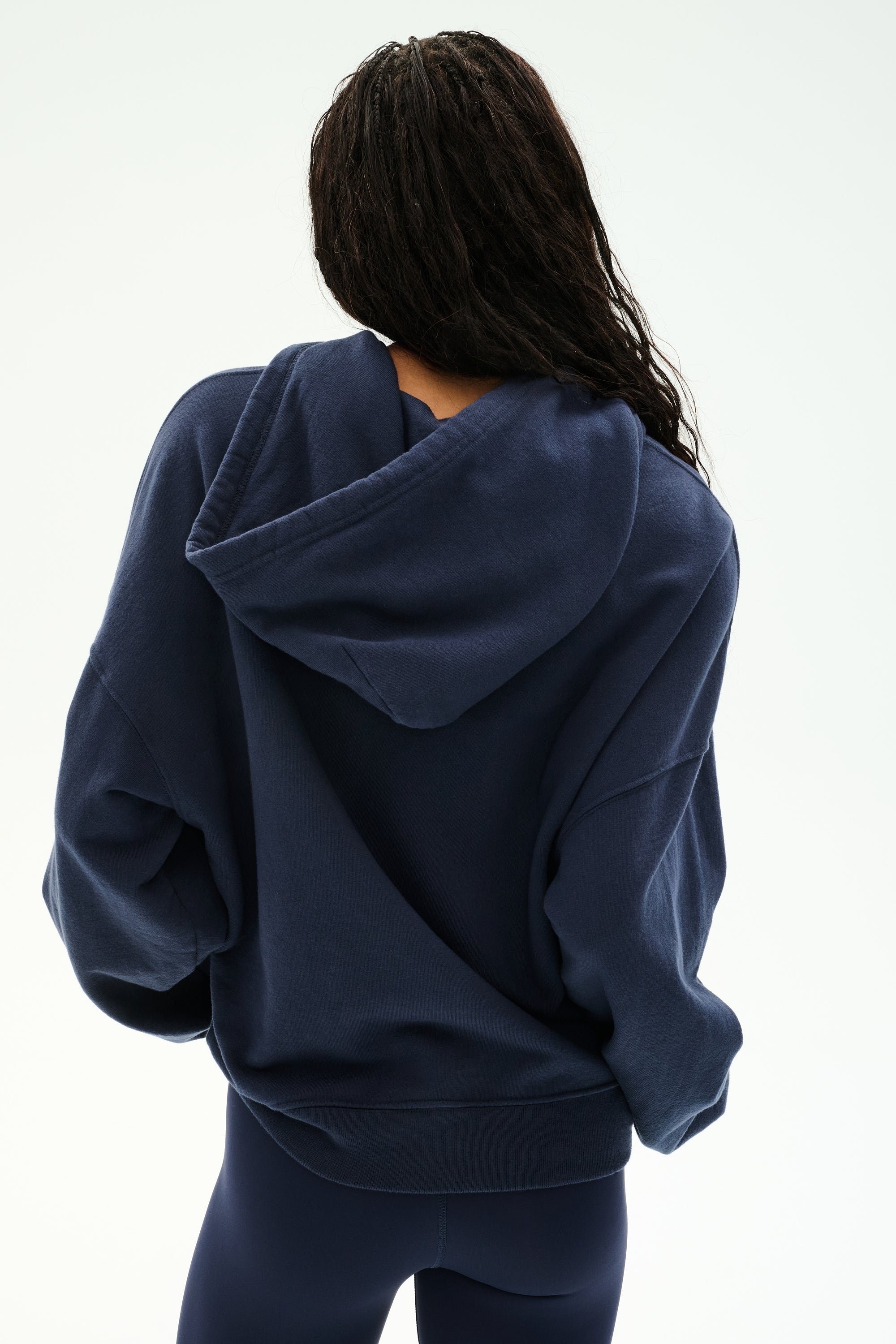 A person is seen from behind against a plain white background, wearing the Stella French Terry Oversized Hoodie in Indigo by SPLITS59 Los Angeles, paired with matching soft cotton leggings.