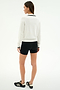 A woman faces away, wearing the SPLITS59 Taylor Knit Polo in White/Black, paired with black shorts and black athletic shoes with white stripes, set against a plain light background.