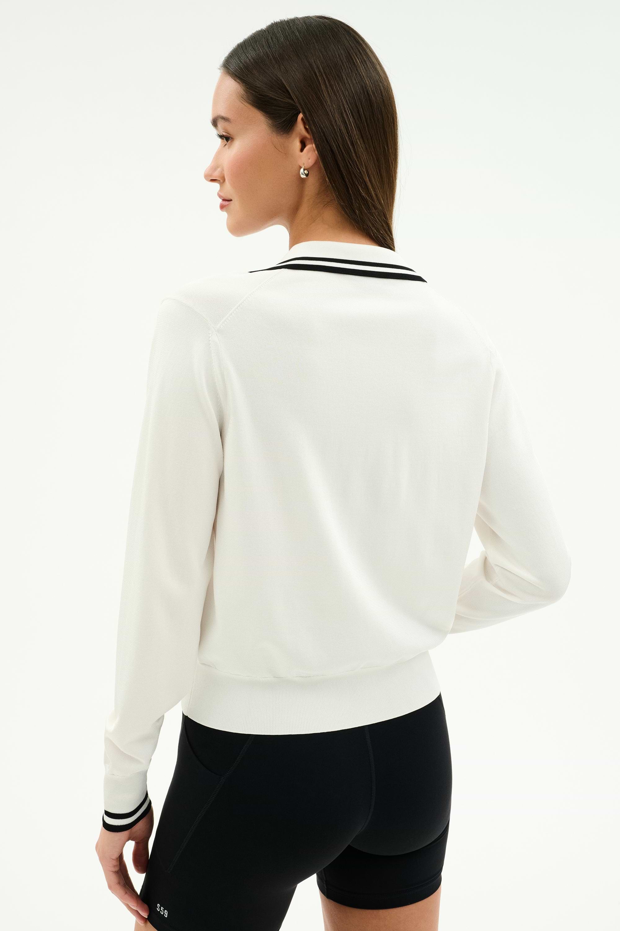 A woman with straight brown hair wears the SPLITS59 Taylor Knit Polo in white/black, paired with black shorts, standing with her back to the camera against a plain background.