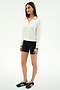A woman stands against a plain background wearing the SPLITS59 Taylor Knit Polo in White/Black, paired with black bike shorts and black sneakers with white stripes.
