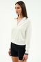 A woman poses against a plain background wearing the SPLITS59 Taylor Knit Polo in white with black stripes, featuring long sleeves and a collared design, styled with fitted black shorts.