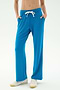 A person wears SPLITS59’s Raven Fleece Full Length Sweatpant in Stone Blue with white sneakers, standing hands-in-pockets against a plain light background.
