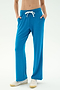 A person wears SPLITS59’s Raven Fleece Full Length Sweatpant in Stone Blue with white sneakers, standing hands-in-pockets against a plain light background.